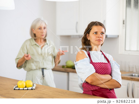 Upset girl at home kitchen while worried elderly mother reprimanding her. Family conflicts concept Upset girl at home kitchen while worried elderly mother reprimanding her. Family conflicts concept 92682218