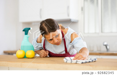 Woman in apron cleaning dinning table with rag in kitchen at home 92682345