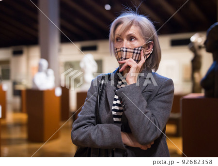 Pensive aged woman in protective mask exploring artworks in museum Pensive aged woman in protective mask exploring artworks in museum 92682358