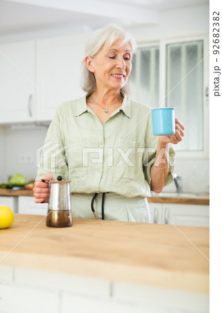 Cheerful senior woman having breakfast with cup of coffee Cheerful senior woman having breakfast with cup of coffee 92682382