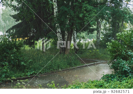 Heavy rain falls on the asphalt in front of grass and trees 92682571
