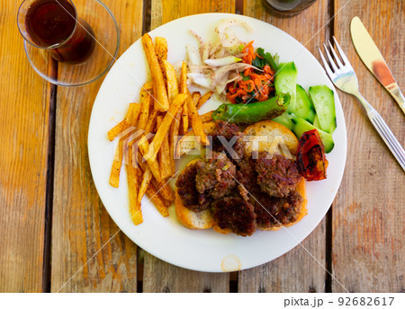 Spicy kofte (grilled minced meat) served with fresh cucumber, bread, vegetables and French fries on rustic wooden board Spicy kofte (grilled minced meat) served with fresh cucumber, bread, vegetables and French fries on rustic wooden board 92682617