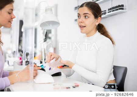 Young female manicurist showing palette of nail varnishes to woman client Young female manicurist showing palette of nail varnishes to woman client 92682646