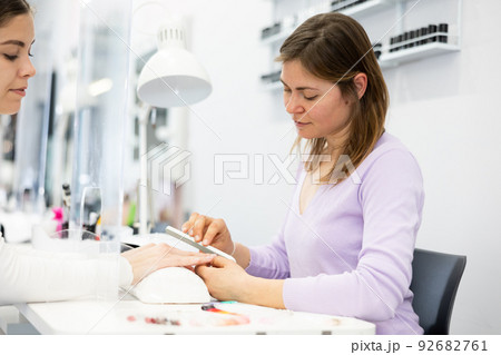 Skilled woman manicure master shaping nails to female client 92682761