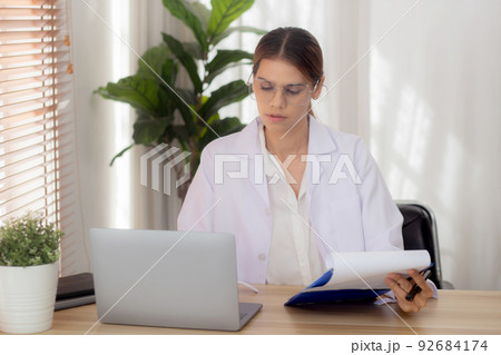 Young woman doctor using laptop computer and looking document paper about patient for diagnostic. Young woman doctor using laptop computer and looking document paper about patient for diagnostic. 92684174