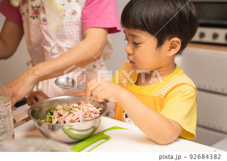 お母さんと二人でボールの中の食材を混ぜ合わせた後、味付けとしてしょうゆを加えようとしている4歳男児 92684382