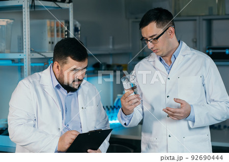 Male scientist with a large flask in his hands. He examines some liquid in a test tube. Working in a scientific laboratory. 92690444