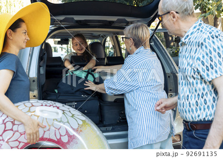 European family travelling on holiday trip, loading trolley bags and inflatable to leave on summer vacation. Parents with small kid and grandparents going on adventure journey with vehicle. 92691135