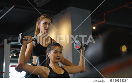 Sporty girl doing weight exercises with the help of her personal trainer at the gym. Sporty girl doing weight exercises with the help of her personal trainer at the gym. 92691884