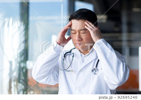 Close-up photo of an Asian doctor tired of work, has a severe headache in the clinic Close-up photo of an Asian doctor tired of work, has a severe headache in the clinic 92695240