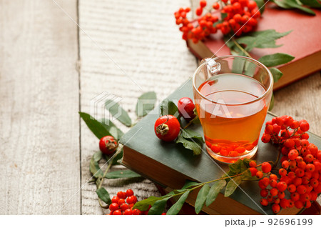 Cup of tea with autumn leaves reflection on book on wooden table. Season of Education, warming rustic rural background, copy space, vitamin beverage for flu, cold Cup of tea with autumn leaves reflection on book on wooden table. Season of Education, warming rustic rural background, copy space, vitamin beverage for flu, cold 92696199