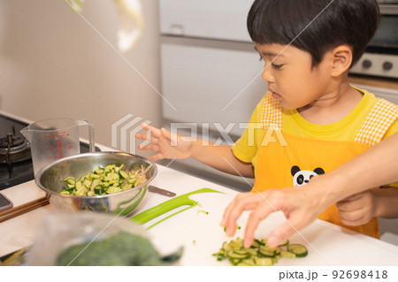 お母さんの料理の手伝いで、ボールにきゅうりを入れる4歳男児 お母さんの料理の手伝いで、ボールにきゅうりを入れる4歳男児 92698418