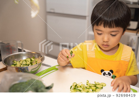 お母さんの料理の手伝いで、きゅうりをボールに入れようとしている4歳男児 お母さんの料理の手伝いで、きゅうりをボールに入れようとしている4歳男児 92698419