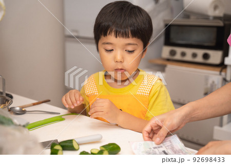 お母さんの料理の手伝いで、きゅうりを切ろうとしている4歳男児 お母さんの料理の手伝いで、きゅうりを切ろうとしている4歳男児 92698433