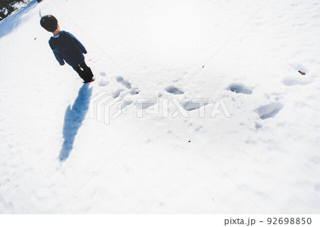 誰も歩いていない雪道を一歩一歩歩いていく子ども 92698850