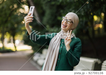 Portrait of smiling happy beautiful muslim woman relaxing using digital smartphone. 92700136