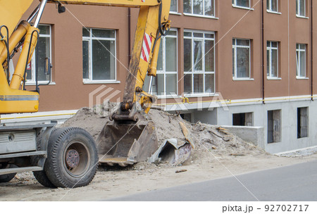 Mobile crane loader of yellow color on the background of a building under construction. German-Swiss international equipment manufacturer. The excavator is used for earthworks. Mobile crane loader of yellow color on the background of a building under construction. German-Swiss international equipment manufacturer. The excavator is used for earthworks. 92702717