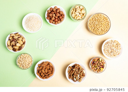 Oval frame of bowls with cereal grains and nuts on two-tone beige-green backdrop. Diet or nutrition concept. Superfoods. Vegan protein source. Healthy food. Top view. Horizontal shot. Copy space. 92705845