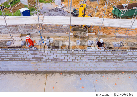 Construction site workers on scaffolding laying masonry cinder concrete blocks 92706666