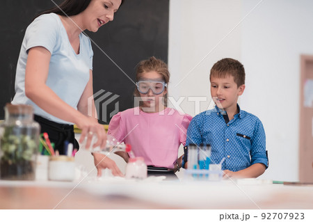 Elementary School Science Classroom: Enthusiastic Teacher Explains Chemistry to Diverse Group of Children, Little Boy Mixes Chemicals in Beakers. Children Learn with Interest Elementary School Science Classroom: Enthusiastic Teacher Explains Chemistry to Diverse Group of Children, Little Boy Mixes Chemicals in Beakers. Children Learn with Interest 92707923