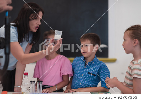 Elementary School Science Classroom: Enthusiastic Teacher Explains Chemistry to Diverse Group of Children, Little Boy Mixes Chemicals in Beakers. Children Learn with Interest 92707969