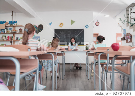 Multiracial group of kids wearing face masks working at class, writing and listening explanations of teacher in classroom Multiracial group of kids wearing face masks working at class, writing and listening explanations of teacher in classroom 92707973