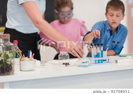 Elementary School Science Classroom: Enthusiastic Teacher Explains Chemistry to Diverse Group of Children, Little Boy Mixes Chemicals in Beakers. Children Learn with Interest Elementary School Science Classroom: Enthusiastic Teacher Explains Chemistry to Diverse Group of Children, Little Boy Mixes Chemicals in Beakers. Children Learn with Interest 92708051