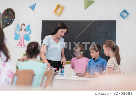 Elementary School Science Classroom: Enthusiastic Teacher Explains Chemistry to Diverse Group of Children, Little Boy Mixes Chemicals in Beakers. Children Learn with Interest 92708083