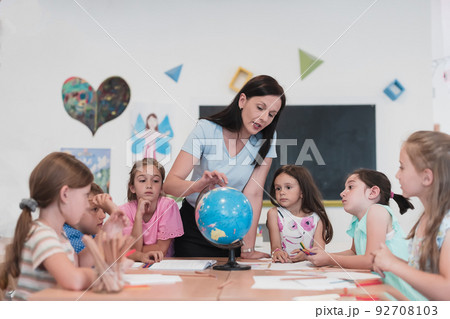 Female teacher with kids in geography class looking at globe. Side view of group of diverse happy school kids with globe in classroom at school. 92708103