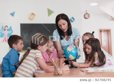 Female teacher with kids in geography class looking at globe. Side view of group of diverse happy school kids with globe in classroom at school. Female teacher with kids in geography class looking at globe. Side view of group of diverse happy school kids with globe in classroom at school. 92708245