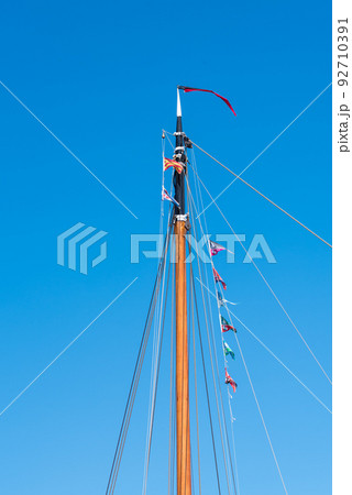 Den Helder, the Netherlands, May 2022. Close up of a mast with flag line against a blue sky. . Den Helder, the Netherlands, May 2022. Close up of a mast with flag line against a blue sky. . 92710391