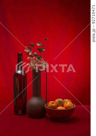 Still life with a bottle, a vase with flowers and apricots 92710471