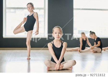 Youthful girl in black leotard sitting on the floor against other performers 92711812