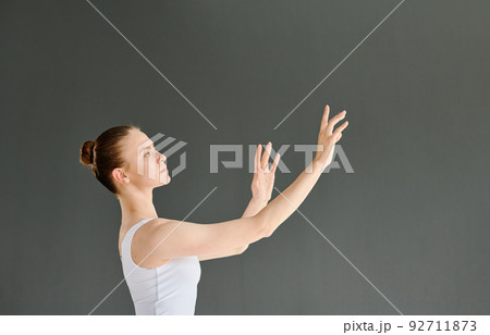 Young ballet dancer in white attire keeping arms raised during exercise 92711873