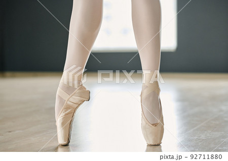 Lower part of slim legs of young ballerina in white tights and pointe shoes Lower part of slim legs of young ballerina in white tights and pointe shoes 92711880