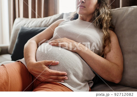 Young pregnant woman keeping hands on her belly while resting on couch 92712082