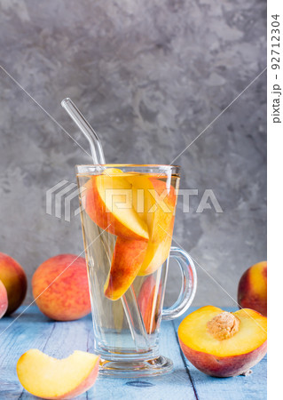 Peach compote in a glass with a straw and fruits on the table. Summer organic drinks. Vertical view Peach compote in a glass with a straw and fruits on the table. Summer organic drinks. Vertical view 92712304