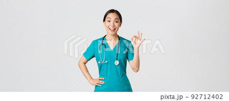 Covid-19, healthcare workers, pandemic concept. Surprised and happy asian female doctor, nurse in scrubs showing okay gesture and smiling amazed, praise nice work, agree with someone Covid-19, healthcare workers, pandemic concept. Surprised and happy asian female doctor, nurse in scrubs showing okay gesture and smiling amazed, praise nice work, agree with someone 92712402