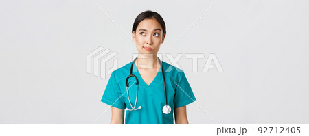 Healthcare workers, preventing virus, quarantine campaign concept. Thoughtful asian female doctor, nurse in scrubs looking upper left corner and smirk unsure, thinking, white background 92712405
