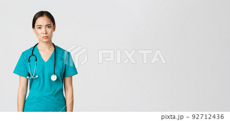 Covid-19, healthcare workers, pandemic concept. Exhausted young asian female nurse, doctor looking tired after shift in hospital, looking sad with fatigue, standing white background in scrubs Covid-19, healthcare workers, pandemic concept. Exhausted young asian female nurse, doctor looking tired after shift in hospital, looking sad with fatigue, standing white background in scrubs 92712436