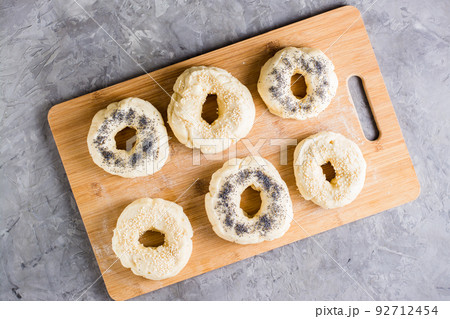 Raw bagels with poppy seeds and sesame seeds on a board on the table. Homemade pastries. Top view Raw bagels with poppy seeds and sesame seeds on a board on the table. Homemade pastries. Top view 92712454