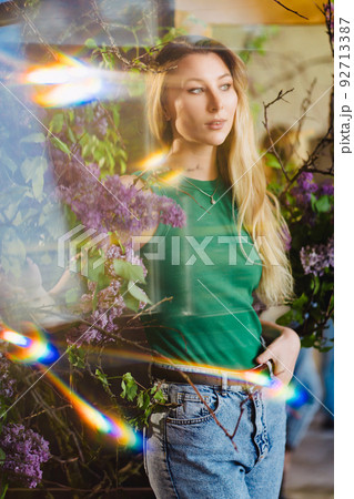 a blonde woman in a green top and jeans with lilac flowers. solar flare. a blonde woman in a green top and jeans with lilac flowers. solar flare. 92713387