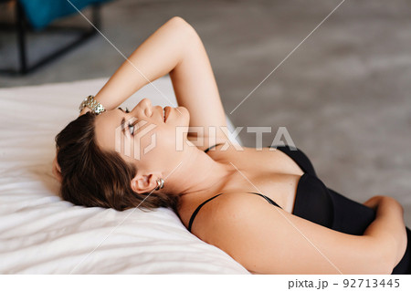 an attractive brunette woman in a black bodysuit by the bed in the bedroom. an attractive brunette woman in a black bodysuit by the bed in the bedroom. 92713445