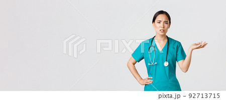 Covid-19, healthcare workers, pandemic concept. Frustrated and annoyed asian female doctor, nurse in scrubs raise one hand and looking questioned and pissed-off, complaining something 92713715