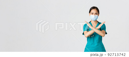 Covid-19, coronavirus disease, healthcare workers concept. Serious displeased, frowning asian doctor in scrubs show cross gesture in disapproval, stop someone, prohibit action, white background Covid-19, coronavirus disease, healthcare workers concept. Serious displeased, frowning asian doctor in scrubs show cross gesture in disapproval, stop someone, prohibit action, white background 92713742