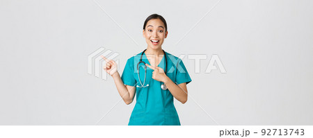 Covid-19, healthcare workers, pandemic concept. Excited asian nurse, doctor in scrubs and stethoscope, pointing fingers upper left corner. Physician smiling amazed as showing awesome announcement Covid-19, healthcare workers, pandemic concept. Excited asian nurse, doctor in scrubs and stethoscope, pointing fingers upper left corner. Physician smiling amazed as showing awesome announcement 92713743