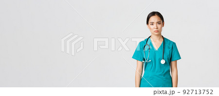 Covid-19, healthcare workers, pandemic concept. Exhausted young asian female nurse, doctor looking tired after shift in hospital, looking sad with fatigue, standing white background in scrubs 92713752