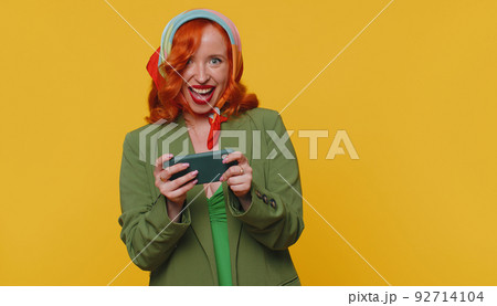 Worried funny addicted redhead girl enthusiastically playing drive racing video game on mobile phone Worried funny addicted redhead girl enthusiastically playing drive racing video game on mobile phone 92714104