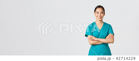 Covid-19, healthcare workers, pandemic concept. Confident smiling asian doctor, female nurse in scrubs standing determined, cross arms chest over white background. Doctor ready for shift in clinic 92714229