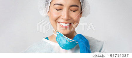 Covid-19, coronavirus disease, healthcare workers concept. Smiling relieved asian female doctor take-off respirator and have skin damage from personal protective equipment, white background 92714387